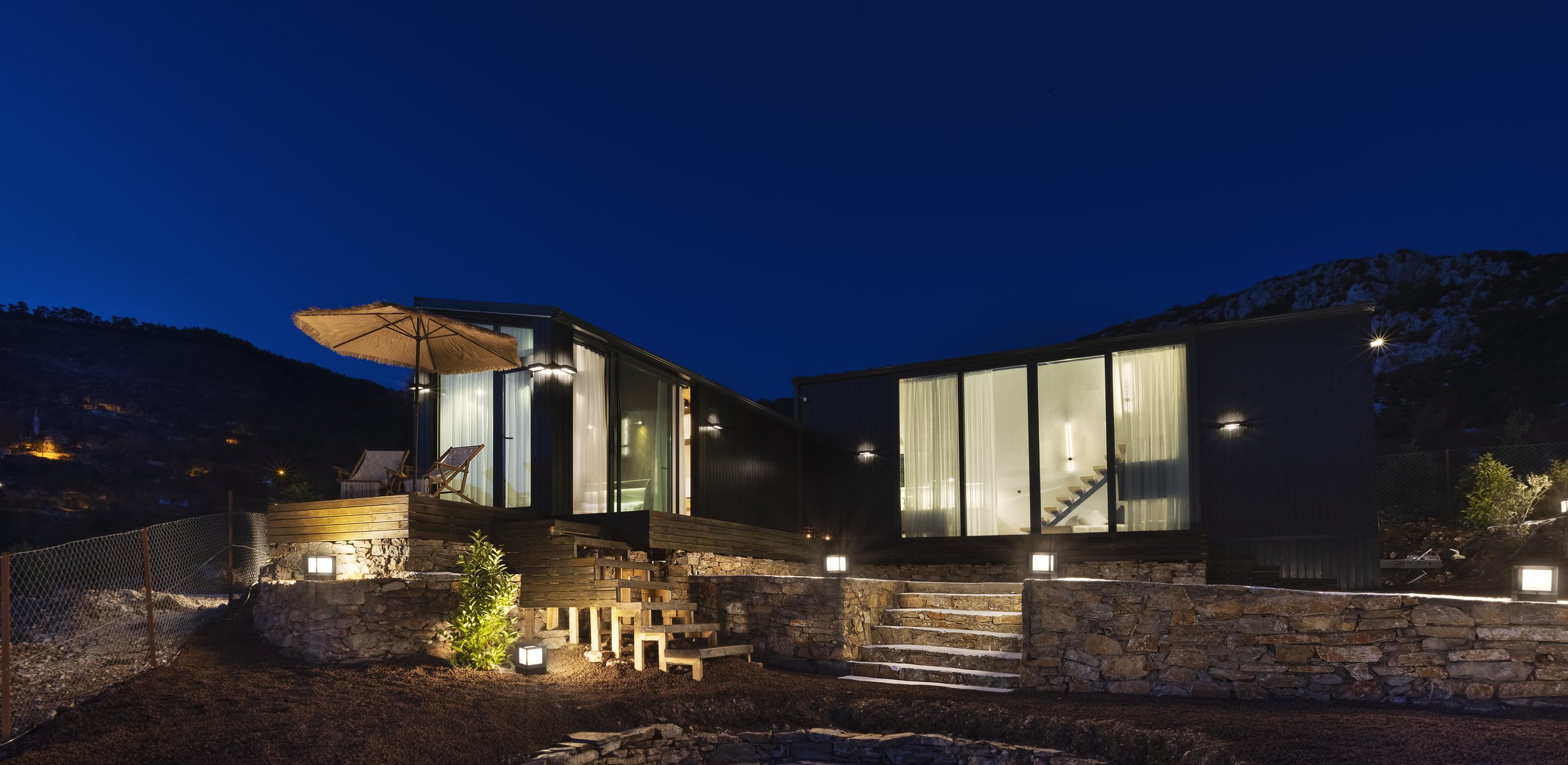 A house at dusk with lit windows and stone terraces, Muğla